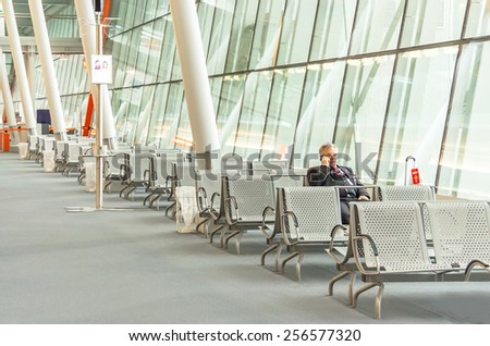 Warsaw, Poland - January 13, 2015. Airport business man with smart phone waiting in terminal for flight. Traveller businessman sitting with luggage suitcase. Caucasian male, air travel concept.