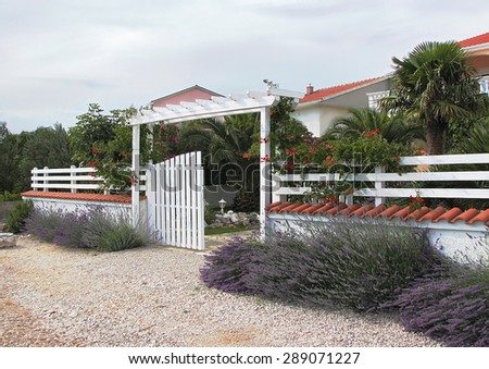 Welcome to relax in a cozy place. White fence, open gate entrance with flowers to the yard (courtyard) and house. Croatia, Dalmatia. Empty place for message. Copy space. Vacation (travel) concept.