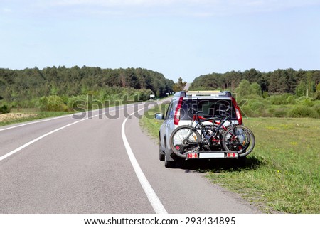 Let\'s go on a trip! The car is by the road and ready to travel. Two bicycles mounted on trunk of jeep. Empty place for message. Copy space. Vacation, freedom, adventure, transportation concept.