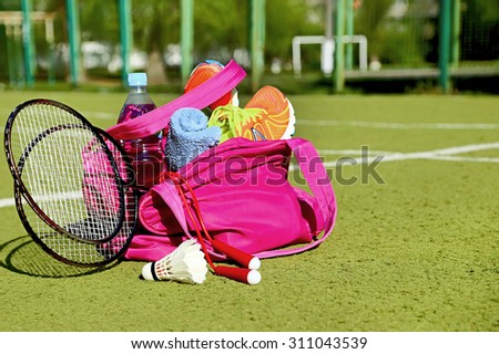 Bag with sports equipment on the sports courts background. Badminton ball (shuttlecock), racket, rope, sneakers, bottle of water, towel are in the bag in the sunny day. Healthy lifestyle. Copy space.