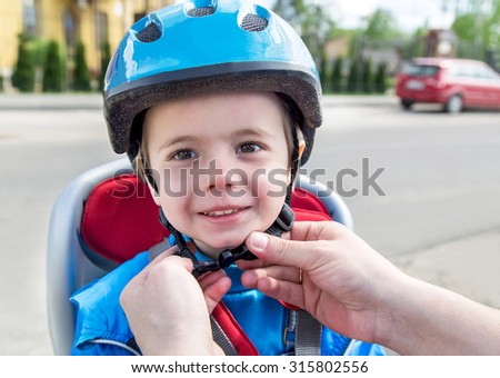 Protection on the bicycle. Caucasian hands of father are putting biking helmet on outside to his son. The son is in the bicycle chair (seat) during bicycle ride. Travel, freedom, adventure  concept.
