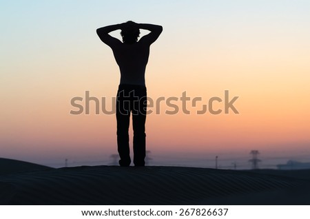 The man silhouette at sunset along in desert with hands behind his head