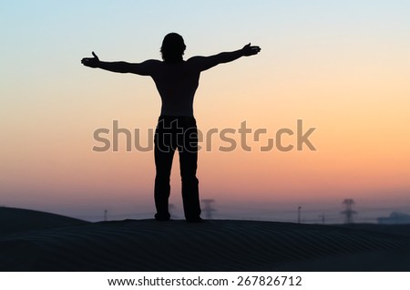 The man silhouette alone at sunset in desert with outstretched arms