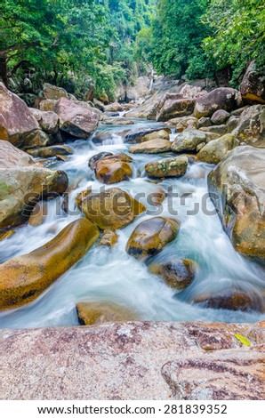 Beautiful photo of waterfalls with soft flowing water and large colored rocks. Green wild jungles on background.