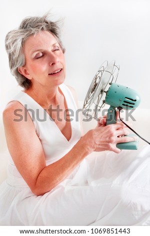 A woman having a hot flash using a fan to cool off.