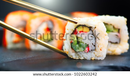 Eating Sushi with chopsticks. Sushi roll japanese food in restaurant. California Sushi roll set with salmon, vegetables, flying fish roe and caviar closeup. Japan restaurant menu
