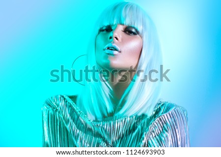 High Fashion model girl in colorful bright neon lights posing in studio, portrait of beautiful woman in white wig and silver trendy glowing make-up. White hair, colorful make up. Glitter neon makeup