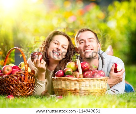 Happy People Eating Organic Apples in Autumn Garden.Healthy Food.Outdoors.Park Basket of Apples.Harvest concept Smiling Couple Relaxing on Grass Happy People Eating Organic Apples in Autumn Garden.Healthy Food.Outdoors.Park Basket of Apples.Harvest concept Smiling Couple Relaxing on Grass