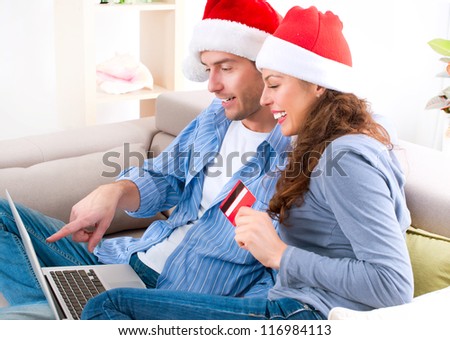 Christmas Shopping On-line . Happy Smiling Couple Using Credit Card to Internet Shop. Young couple with laptop and credit card buying online. Christmas and New Year Gifts. e-shopping