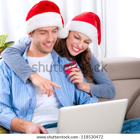 Christmas Online Shopping. Happy Smiling Couple Using Credit Card to Internet Shop. Young couple with laptop and credit card buying online. Christmas and New Year Gifts. e-shopping