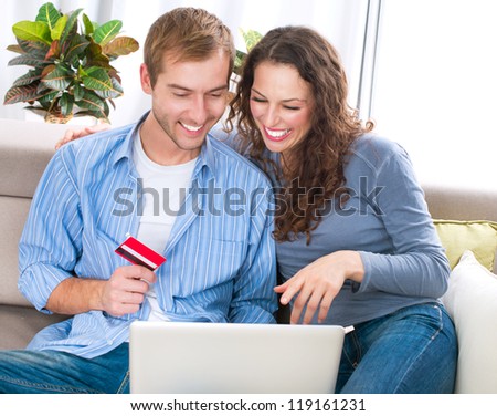 Online Shopping. Happy Smiling Couple Using Credit Card to Internet Shop on-line. Young couple with Laptop Computer and Credit Card buying online. Christmas and New Year Gifts. e-shopping