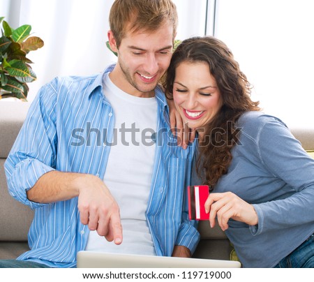 Online Christmas Shopping.Happy Smiling Couple Using Credit Card to Internet Shop on-line. Young couple with Laptop Computer and Credit Card buying online. Christmas and New Year Gifts. e-shopping