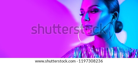 High Fashion model girl in colourful bright neon uv lights posing in studio, portrait of beautiful woman, trendy glowing metallic make-up, silver accessories earrings. Vivid neon makeup. Wide angle