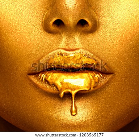 Gold Paint drips from the lips, lipgloss dripping from sexy lips, golden liquid drops on beautiful model girl\'s mouth, gold metallic skin make-up. Beauty woman face makeup close up.