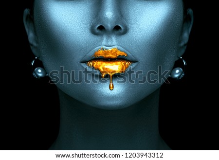 Gold Paint drips from the lips, lipgloss dripping from sexy lips, golden liquid drops on beautiful model girl\'s mouth, creative abstract dark blue skin make-up. Beauty woman face makeup close up.
