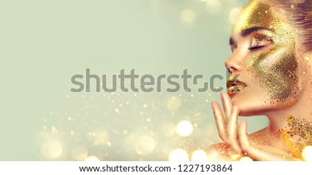 Beauty fashion model girl with Golden skin make up and body, golden jewellery background. Gold body art. Metallic, glance beautiful lady touching face. Border Fashion art portrait, make up, gift