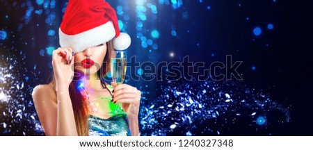 Christmas sexy woman. Beauty model girl in Santa Claus hat with red lips, champagne glass in her hand Celebrating on night club party. Closeup glamour portrait on winter wide background with copyspace