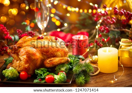 Christmas Dinner. Roasted chicken. Winter Holiday table served, decorated with candles. Roast turkey over wooden background with Christmas tree, table setting. Winter holiday Xmas food