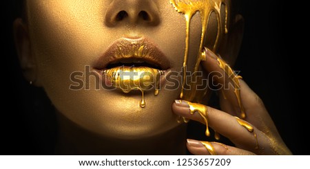 Gold Paint smudges drips from the face lips and hand, lipgloss dripping from sexy lips, golden liquid drops on beautiful model girl\'s mouth, gold metallic skin make-up. Beauty woman makeup close up.