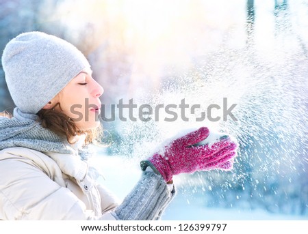 Beautiful Winter Woman Blowing Snow outdoor. Beauty Girl Having Fun in Winter Park. Outdoors. Snowflakes