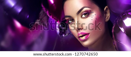 Beauty fashion model girl creative art makeup, over purple, pink and violet air balloons background. Woman face Make-up with gems, pink with gold lips, purple eyeshadows. Widescreen