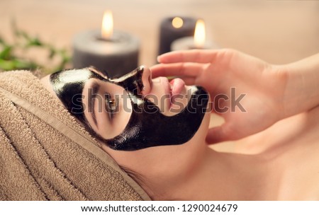 Beautiful woman with black purifying black mask on her face. Beauty model girl with black facial peel-off mask lying in spa salon. Skin care, acne treatment, cleansing   skin. Peel of charcoal mask