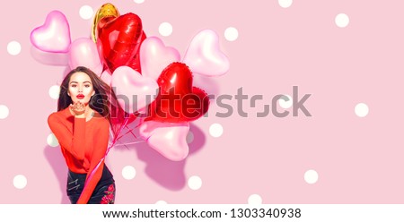 Valentine Beauty girl with colorful air balloons laughing, on pink background. Beautiful Happy Young woman. holiday party. Joyful model having fun, playing and celebrating with red color balloon