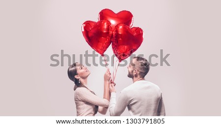 Valentine Couple. Portrait of Smiling Beauty Girl and her Handsome Boyfriend holding bunch of heart shaped air balloons and laughing. Happy Joyful Family. Love. Happy Valentine\'s Day