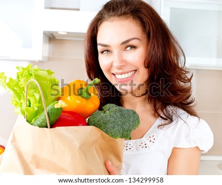 Happy Young Woman With Vegetables In Shopping Bag . Beauty Girl In The Kitchen Cooking Healthy Food. Diet Concept