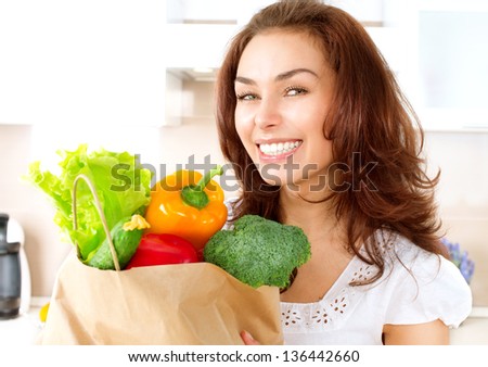 Happy Young Woman with vegetables in shopping bag . Beauty Girl in the kitchen Cooking healthy Food. Diet Concept