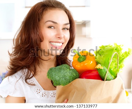 Happy Young Woman with vegetables in shopping bag . Beauty Girl in the kitchen Cooking healthy Food. Diet Concept