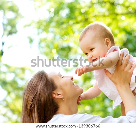 Beautiful Mother And Baby outdoors. Nature. Beauty Mum and her Child playing in Park together. Outdoor Portrait of happy family. Mom and Baby portrait