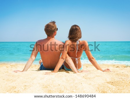 Young Couple Sitting together on the Beach. Sand by Sea. Travel and Vacation concept. Young Family Relaxing and Enjoying their Summer Holidays