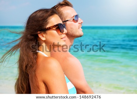Happy Couple in Sunglasses having fun on the Beach. Summer Vacation. Laughing Family enjoying Nature over Sea Background. Attractive Man and Woman at the Beach