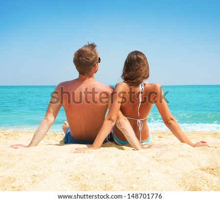 Young Couple Sitting together on the Beach. Sand by Sea. Travel and Vacation concept. Young Family Relaxing and Enjoying their Summer Holiday