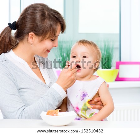 Mother Feeding Her Baby Girl with a Spoon. Mother Giving Food to her adorable Child at Home