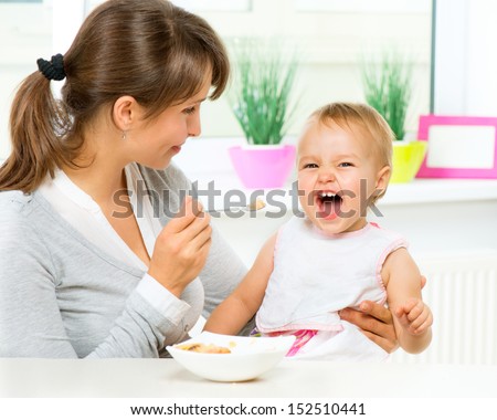 Mother Feeding Her Baby Girl with a Spoon. Mother Giving Food to her adorable Child at Home