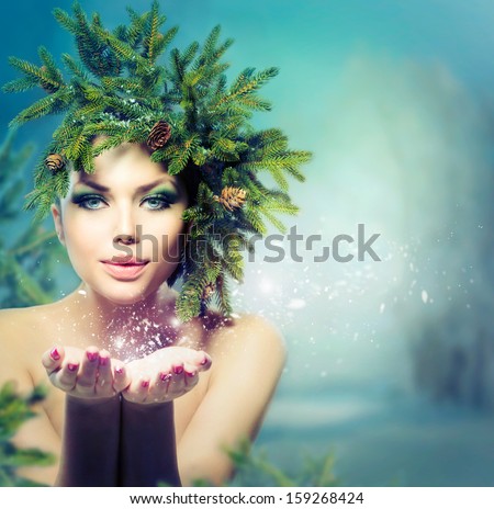 Winter Christmas Woman. Beautiful New Year and Christmas Holiday Girl Blowing Snow. Snowflakes. Hairstyle and Make up. Beauty Fashion Model Girl with Christmas Tree Hairstyle
