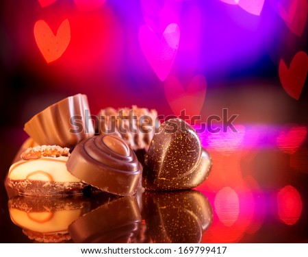 Valentine Chocolates. Assorted Chocolate Candies. Chocolate Sweets. Candy Border Design over Purple Hearts Bokeh Background. Heart Shaped Chocolate