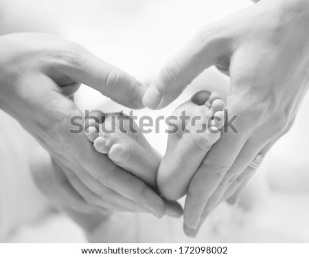 Baby feet in mother hands. Tiny Newborn Baby\'s feet on female Heart Shaped hands closeup. Mom and her Child. Happy Family concept. Beautiful Black and White conceptual image of Maternity