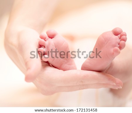 Baby feet in mother hands. Tiny Newborn Baby\'s feet on female hands closeup. Mom and her Child. Beautiful Soft Conceptual image of Maternity