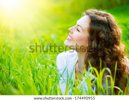 Beautiful Spring Young Woman Outdoors Enjoying Nature. Healthy Smiling Girl In Green Grass. Spring Meadow. Beautiful Lady Lying On The Field