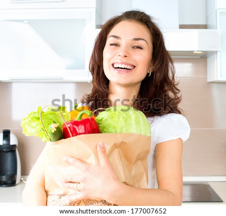 Happy Young Woman with vegetables in shopping bag. Beauty Girl in the kitchen Cooking healthy Food. Diet Concept. Young woman holding grocery shopping bag with vegetables. Healthy eating concept