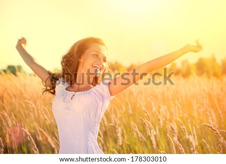 Beauty Girl Outdoors Enjoying Nature. Beautiful Teenage Model Girl In White Dress Running On The Spring Field, Sun Light. Glow Sun. Free Happy Woman. Toned In Warm Colors.