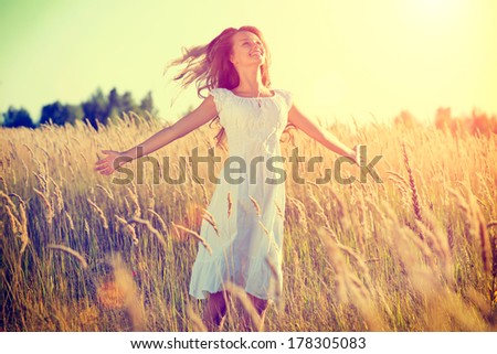 Beauty Girl Outdoors enjoying nature. Beautiful Teenage Model girl in white dress running on the Spring Field, Sun Light. Glow Sun. Free Happy Woman. Toned in warm colors.