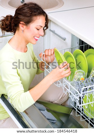 Dishwasher. Happy Young woman in the Kitchen doing Housework. Dishwasher Machine, dishwashing. Wash-up. Smiling Girl using dishwasher machine