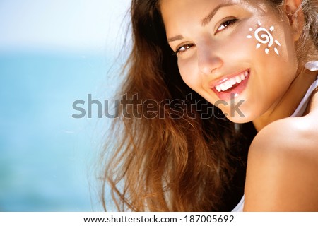 Suntan Lotion Woman Applying Sunscreen Solar Cream. Beautiful happy cute Girl applying Sun Tan Cream on her Face over ocean background. Sun Tanning. Skin care and Protection. Vacation