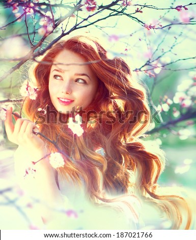 Spring beauty girl with long red blowing hair outdoors. Blooming trees. Romantic young woman portrait. Nature