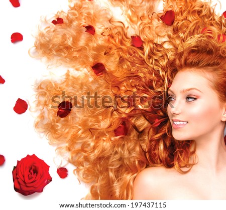 Beauty model girl with healthy long curly red hair and beautiful hairstyle decorated with red roses petals. Fashion woman with Wavy healthy hair isolated on white background.