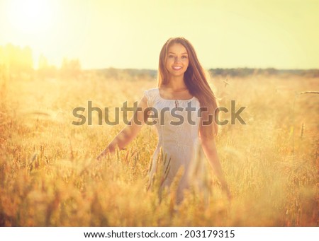 Beauty Girl Outdoors enjoying nature. Beautiful Teenage Model girl in white dress running on the Field, Sun Light. Glow Sun. Free Happy Woman. Toned in warm colors. Autumn